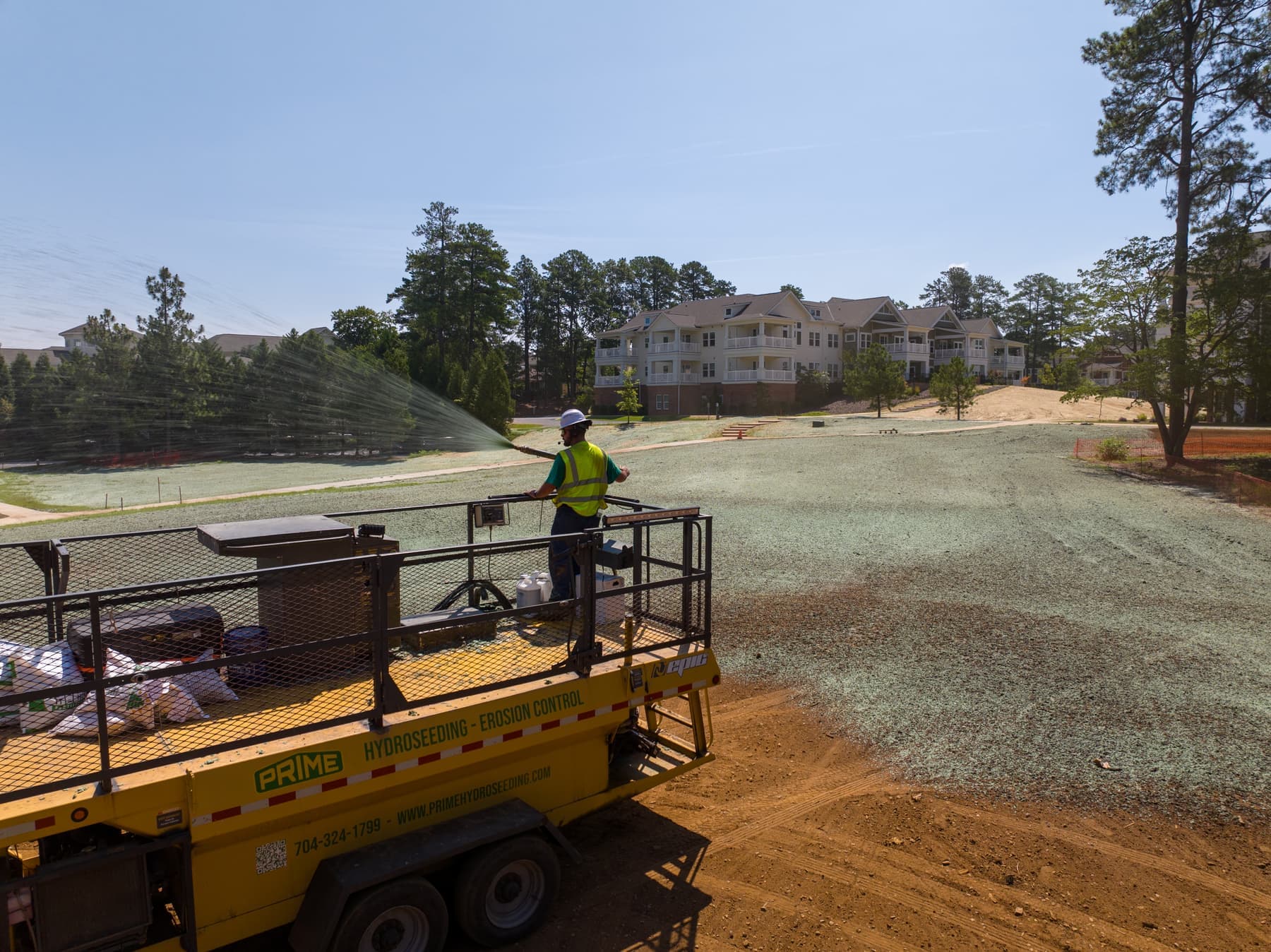 Prime Hydroseeding crew member on a lift applying hydroseed near a multifamily apartment complex