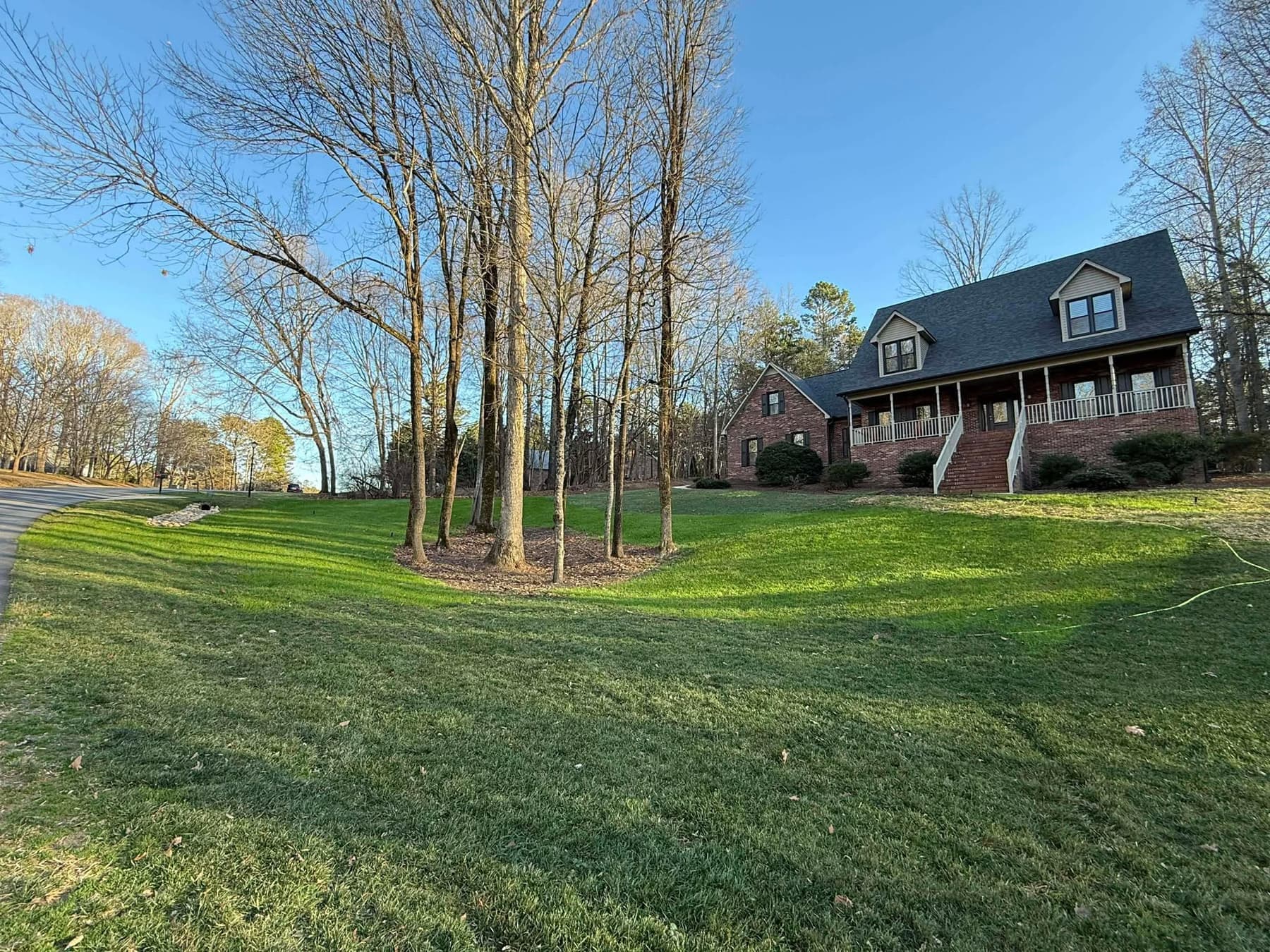 Established green front lawn at a brick residential home with a tree island