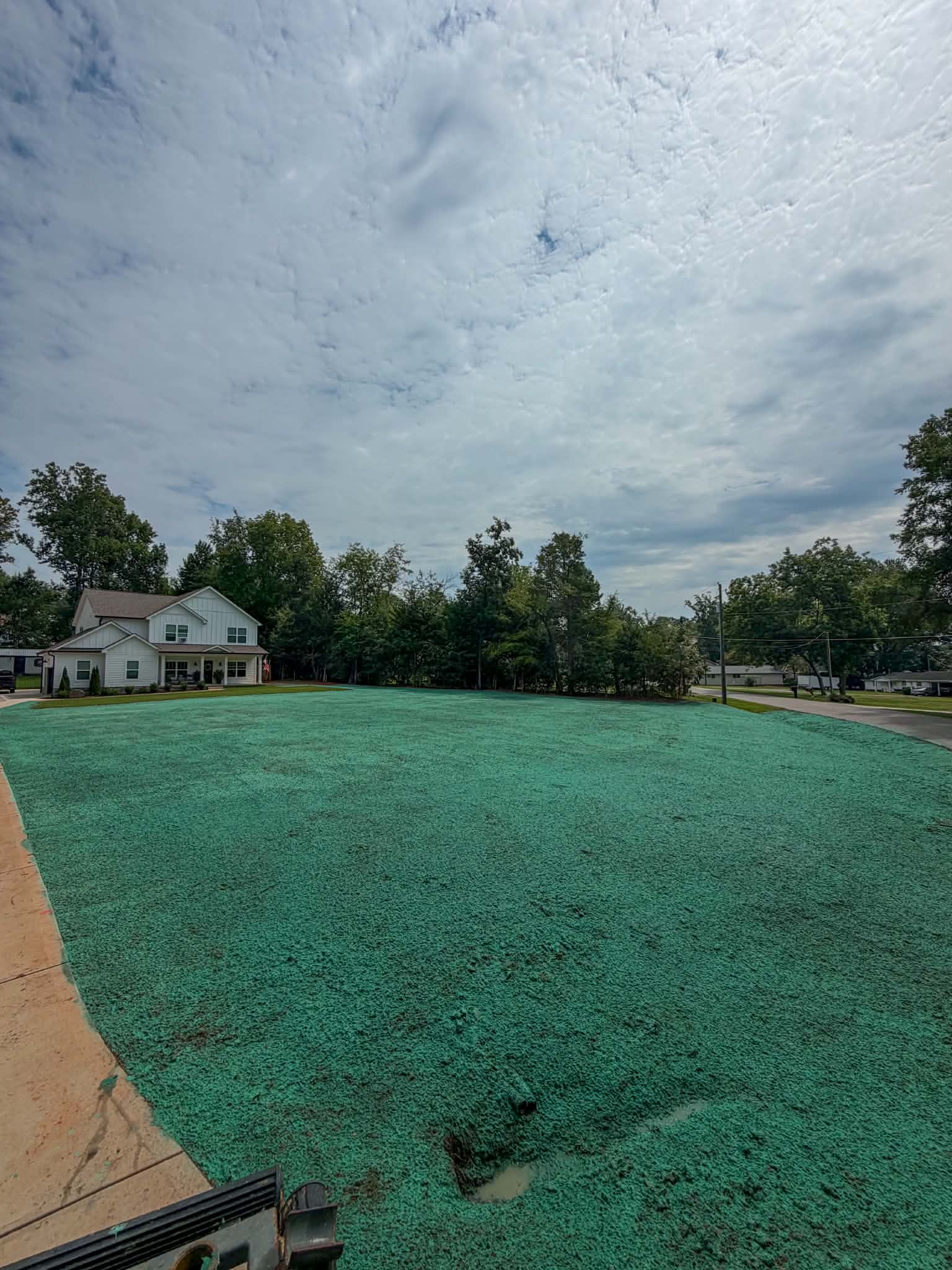 Freshly hydroseeded yard at a farmhouse-style new construction home under a cloudy sky