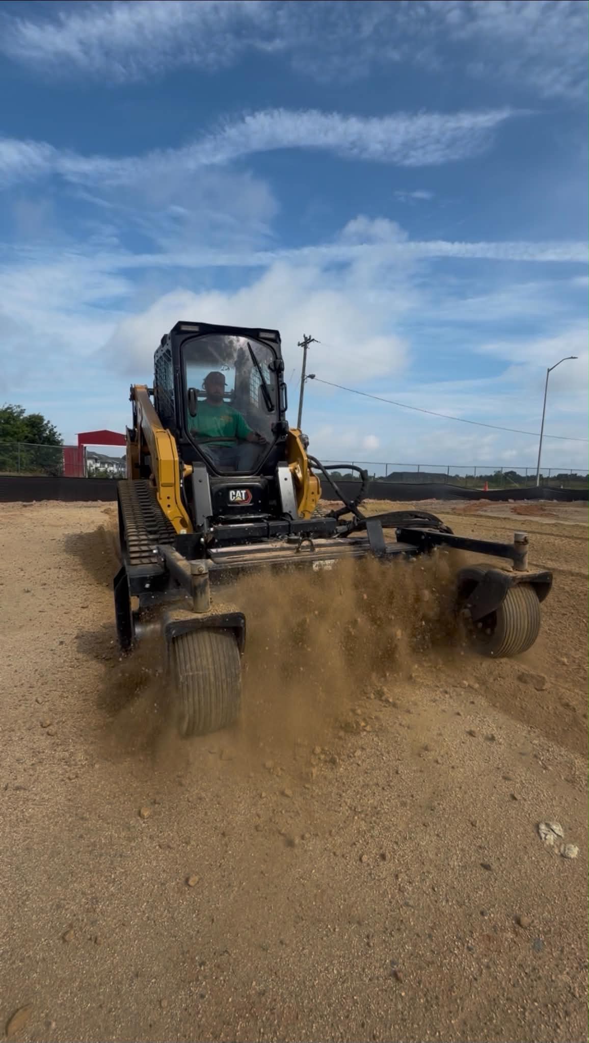 Skid steer with a rotary rake attachment finish-grading a construction site before seeding